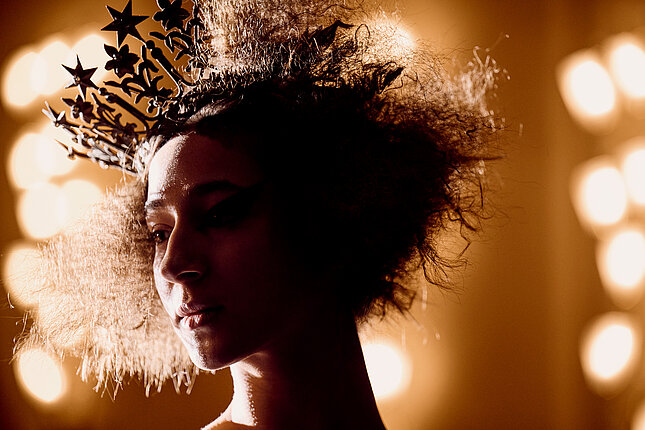 Portrét tanečnice s krátkými kudrnatými vlasy a korunkou na hlavě.