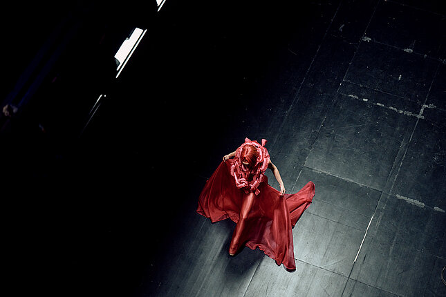 Tanečnice s červenými vlasy a v červených šatech přechází po jevišti.