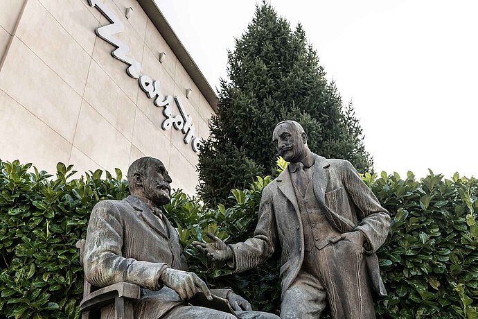 Dva muži v oblecích jako bronzové sochy před budovou Marzotto.